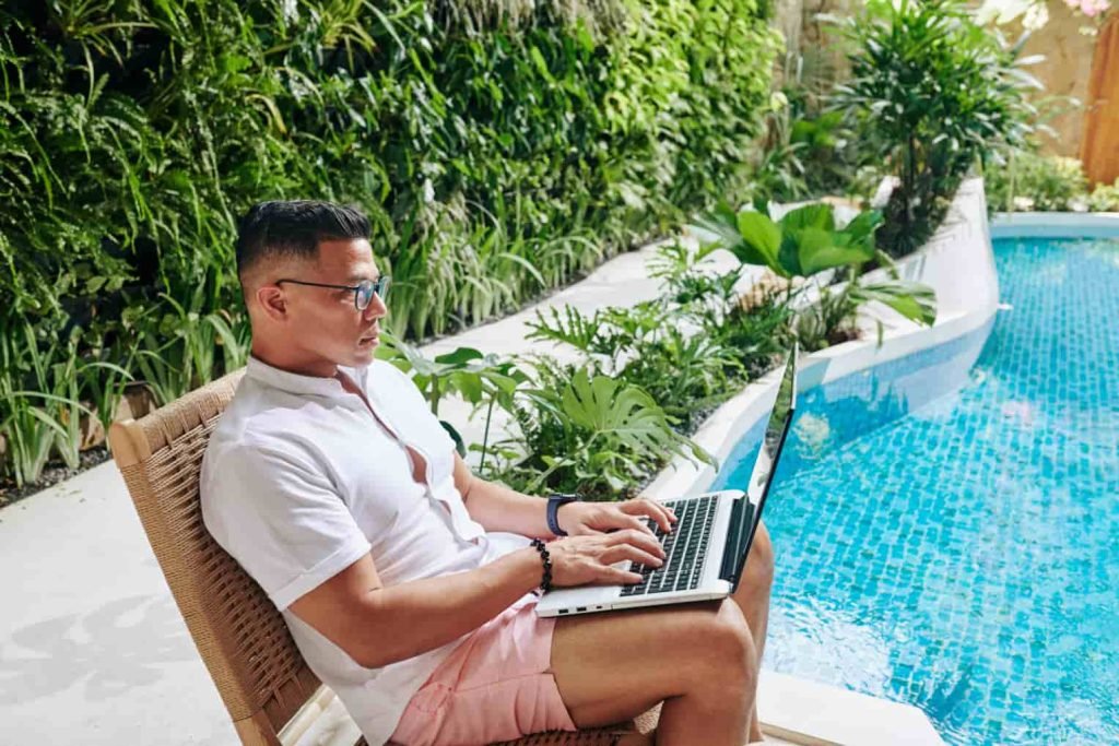 digital nomad working on his laptop at the poolside